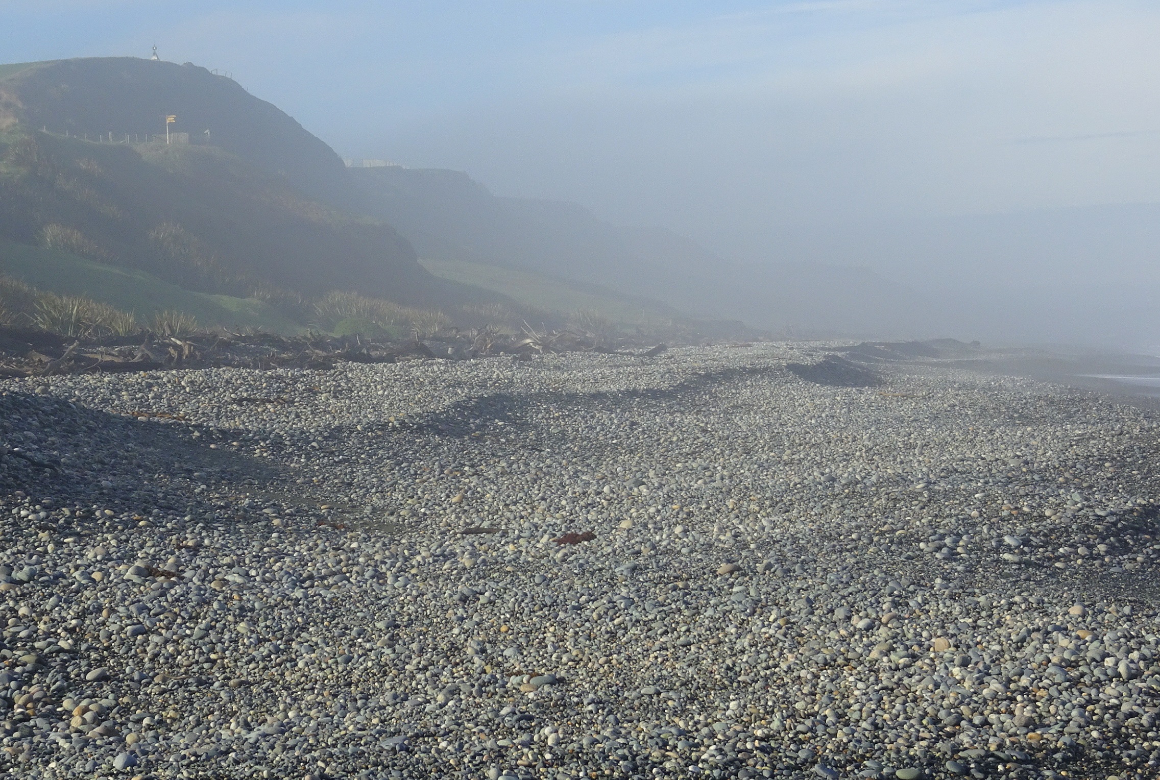 The lookout can just be seen top left. Lots of stones on the beach, many quite large.