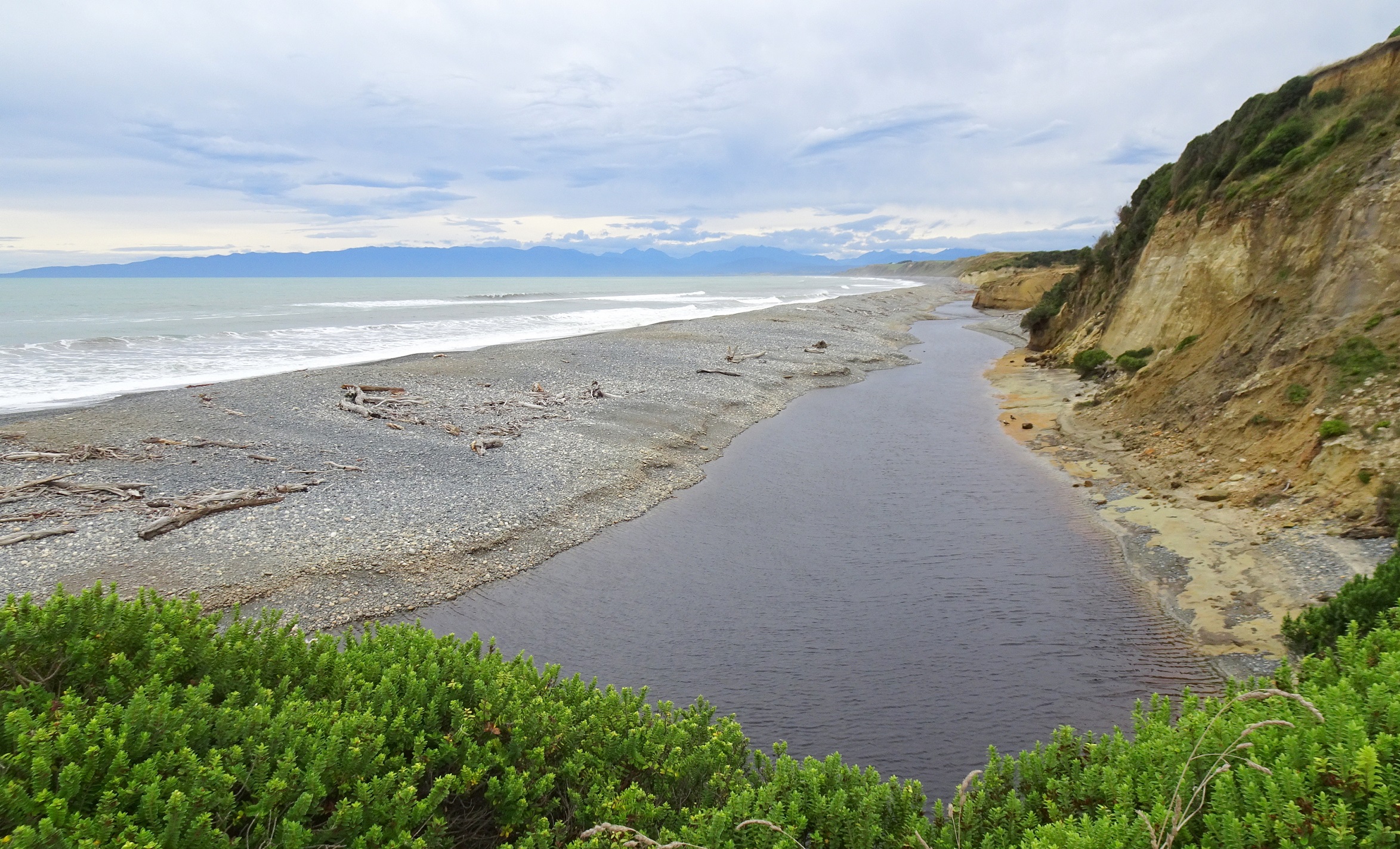 The lagoon of the Waimeamea/Waimehameha River running behind a large bank of stones before flowing across the beach to the sea.