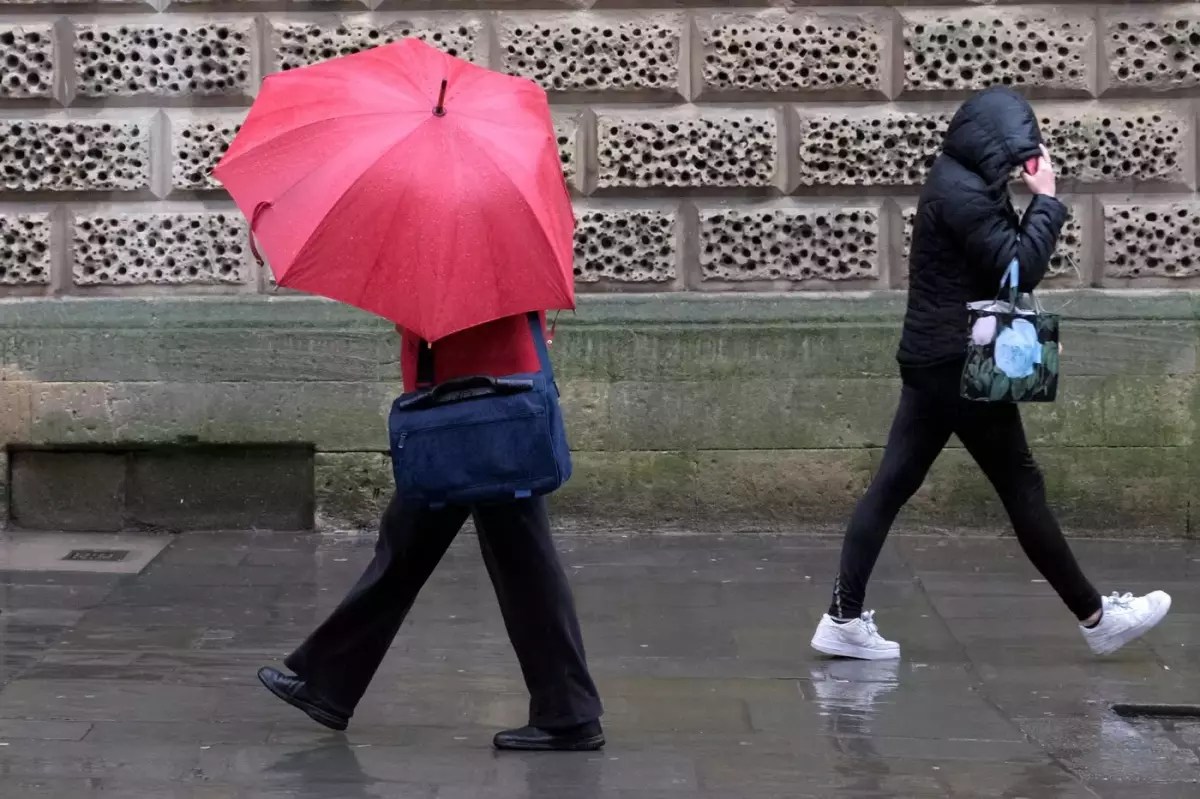 Două persoane merg pe trotuar ploios, una cu umbrelă roz