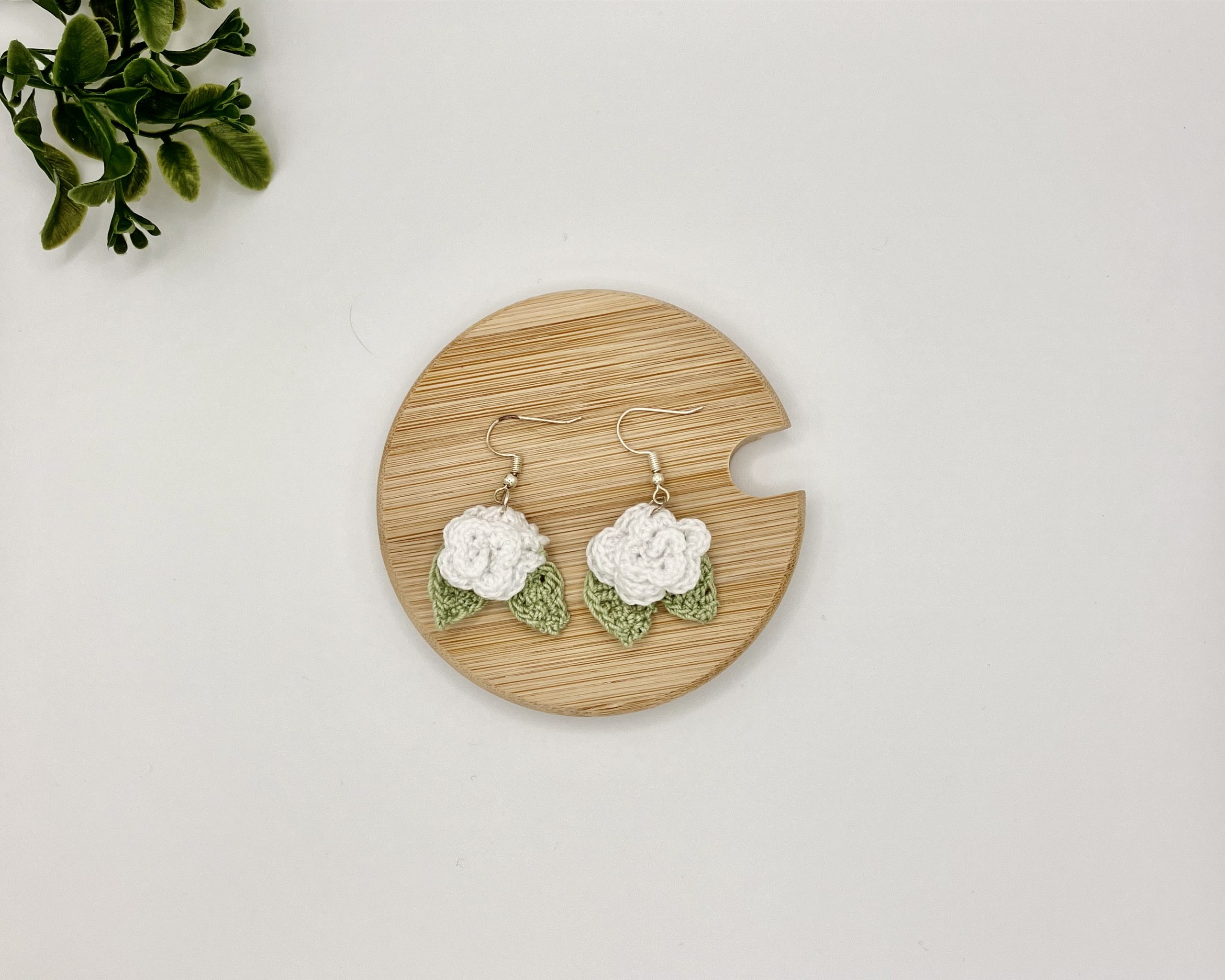 Crochet white rose earrings laying flat on a wood backdrop