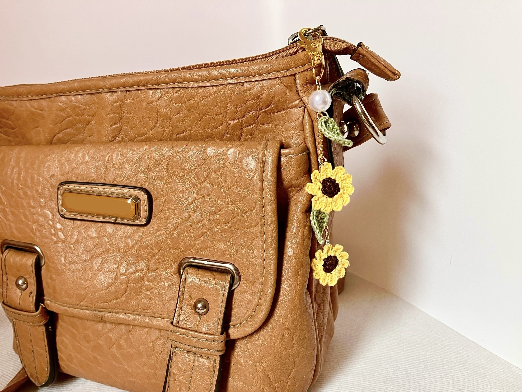 Crochet sunflower bag charm with two sunflowers, pearl accent, and leaves, on a brown purse