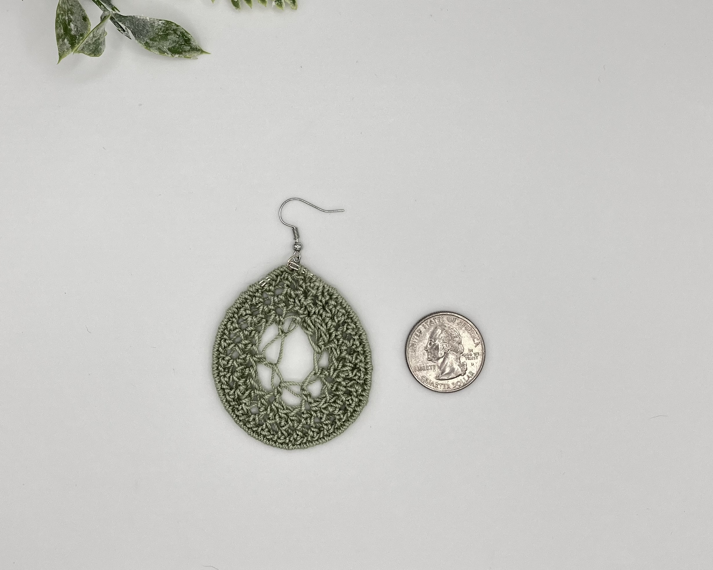 A crochet green dream catcher earring laying next to a quarter for reference