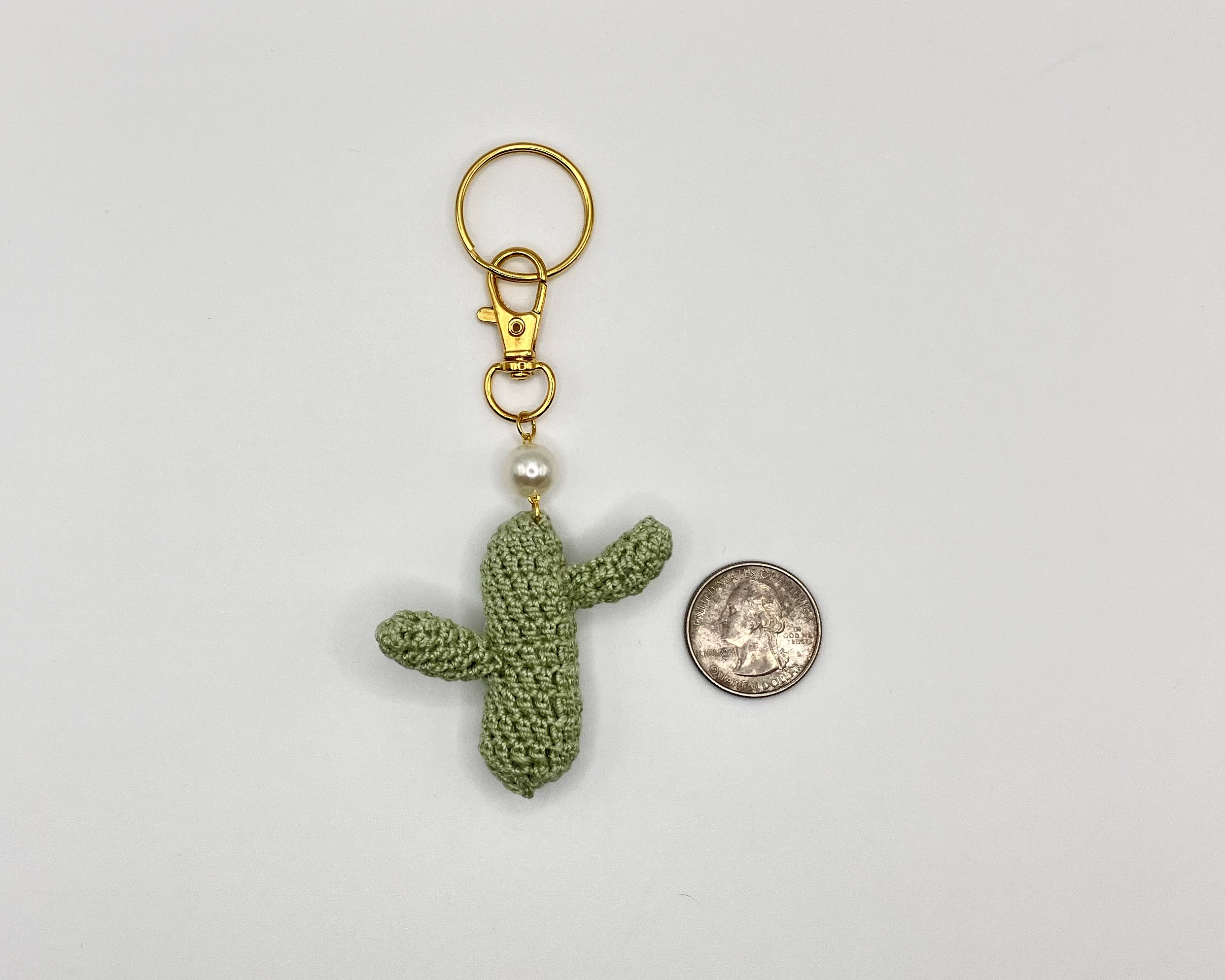 Crocheted green cactus with pearl accent, and gold key ring, next to a quarter for size reference