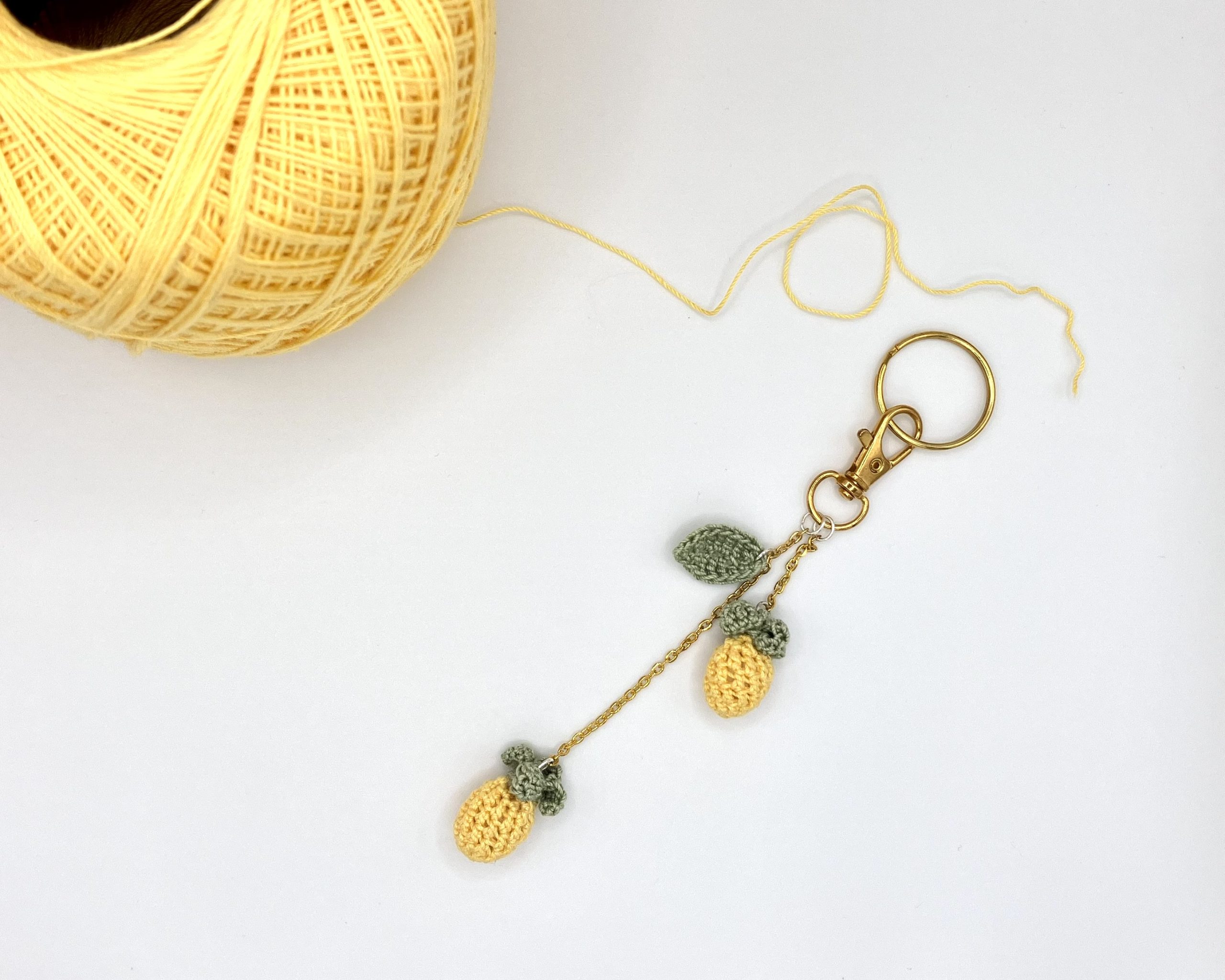 Crocheted pineapple bag charm next to a ball of yellow yarn