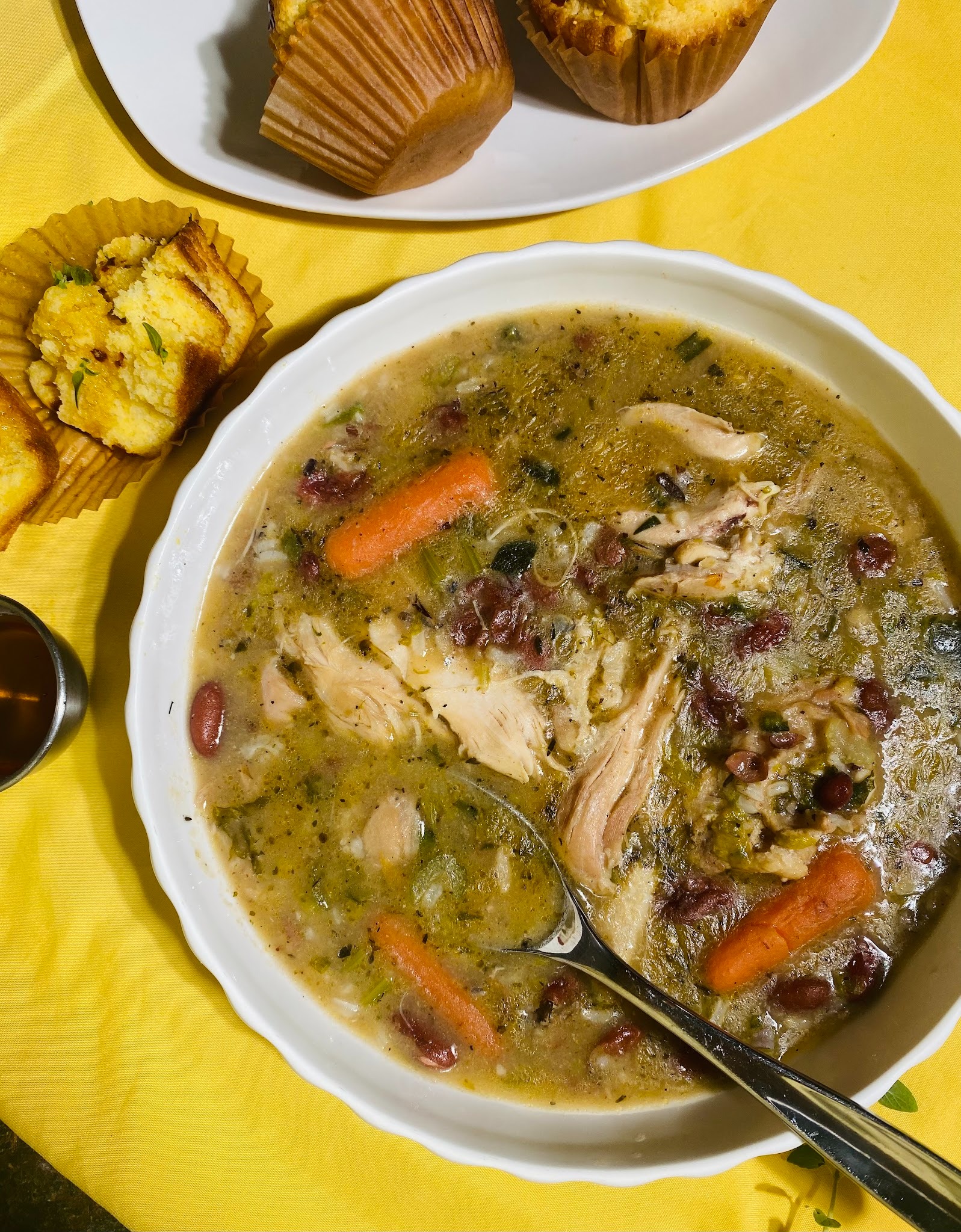 Overhead shot of the chicken and red bean soup with baby carrots on. Yellow background corn muffins in the left corner