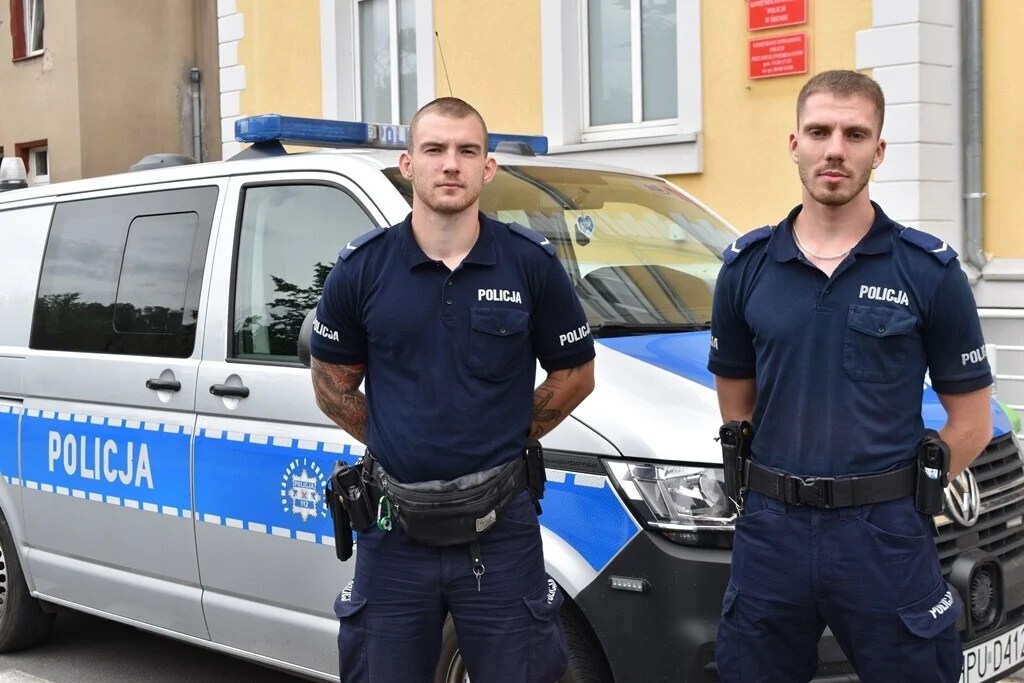 dwaj funkcjonariusze policji w umundurowaniu na tle radiowozu