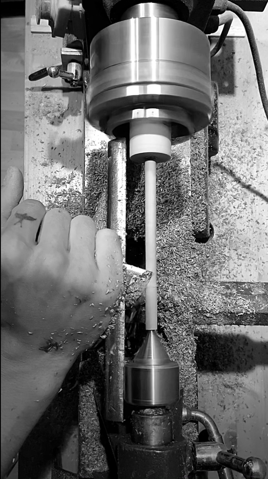 Nahaufnahme einer Hand, die eine Drehmaschine bedient, mit Holzspänen und dem Schneidwerkzeug der Maschine in Aktion.