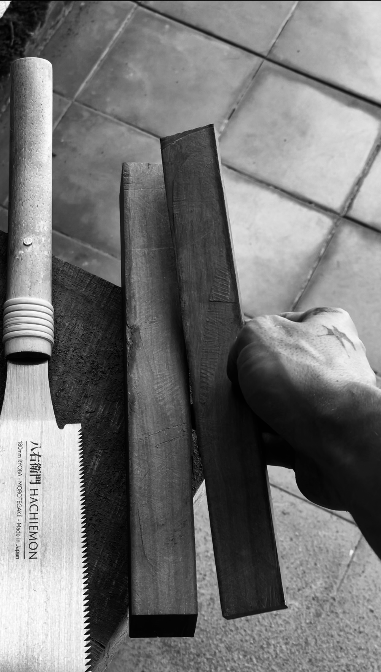 Eine Nahaufnahme, die eine Hand zeigt, die drei Holzstücke neben einer Säge auf einer Arbeitsfläche hält.