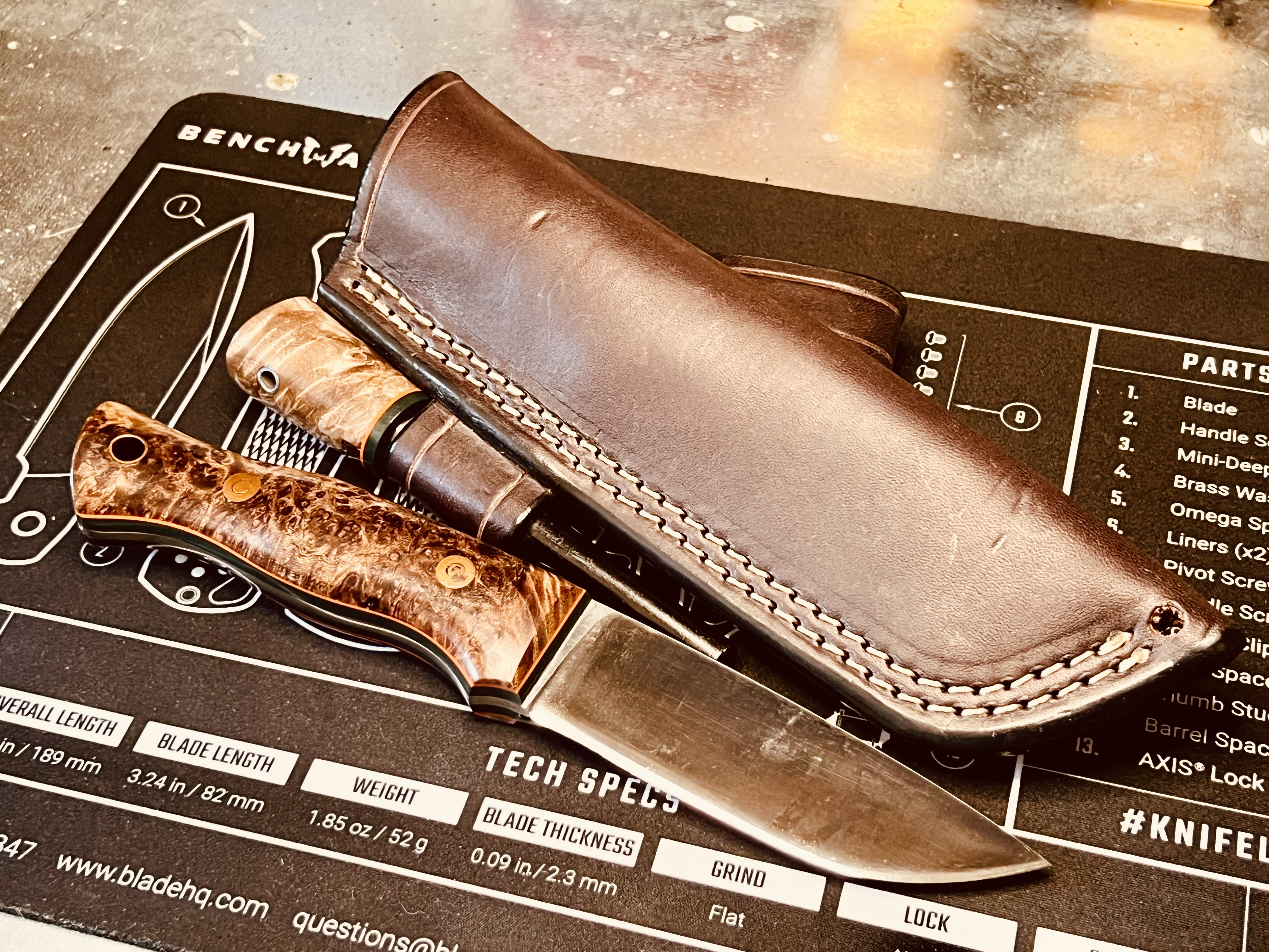 Adventure Sworn Huntsman knife, matching firesteel and dark brown leather sheath on a bench mat.