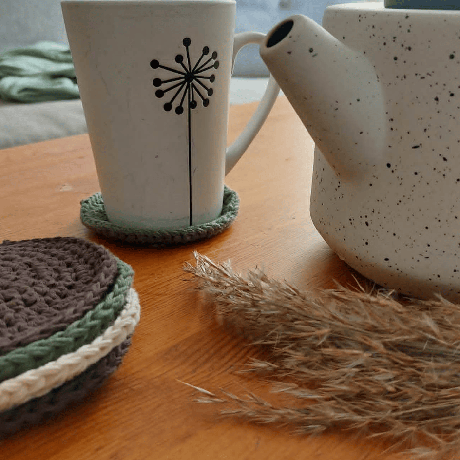 crocheted coasters on a table with a tea pot and a tea cup on top of a cup coaster