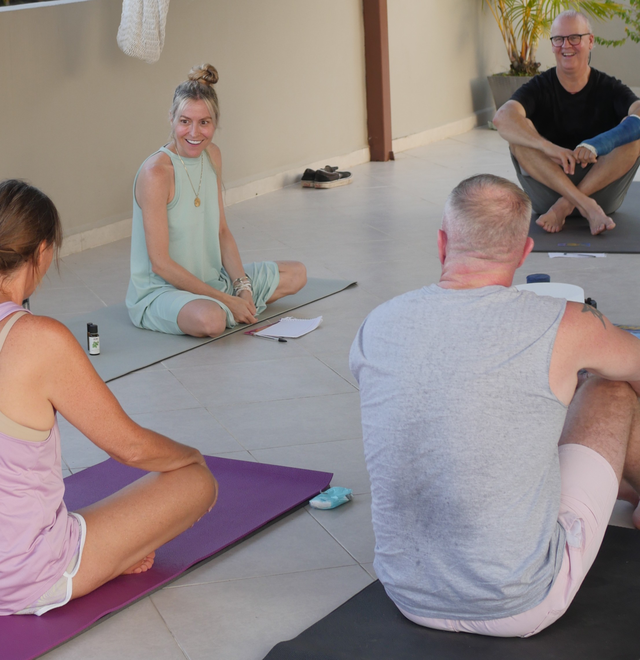 Group of adults seated on yoga mats, chatting and smiling during a relaxed yoga session.