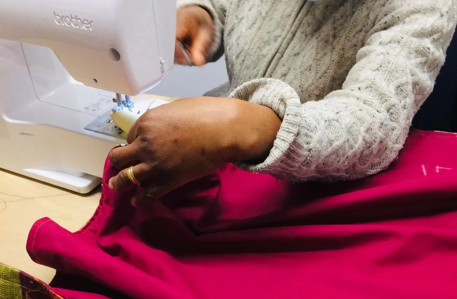 A closeup of a Black woman's hands using the sewing machine in a red fabric