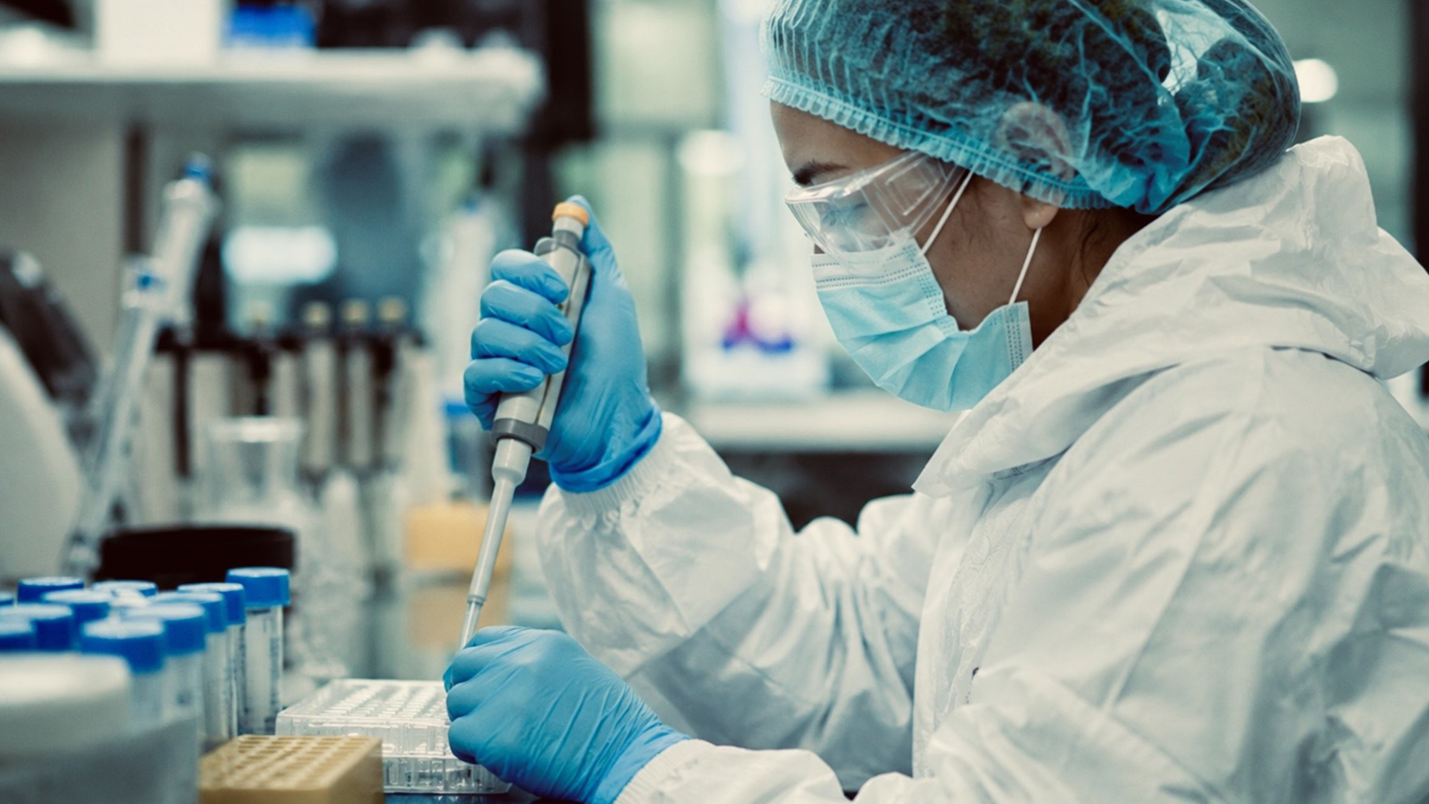 Laboratory researcher in protective medical equipment handling samples during infectious disease testing and outbreak investigation.