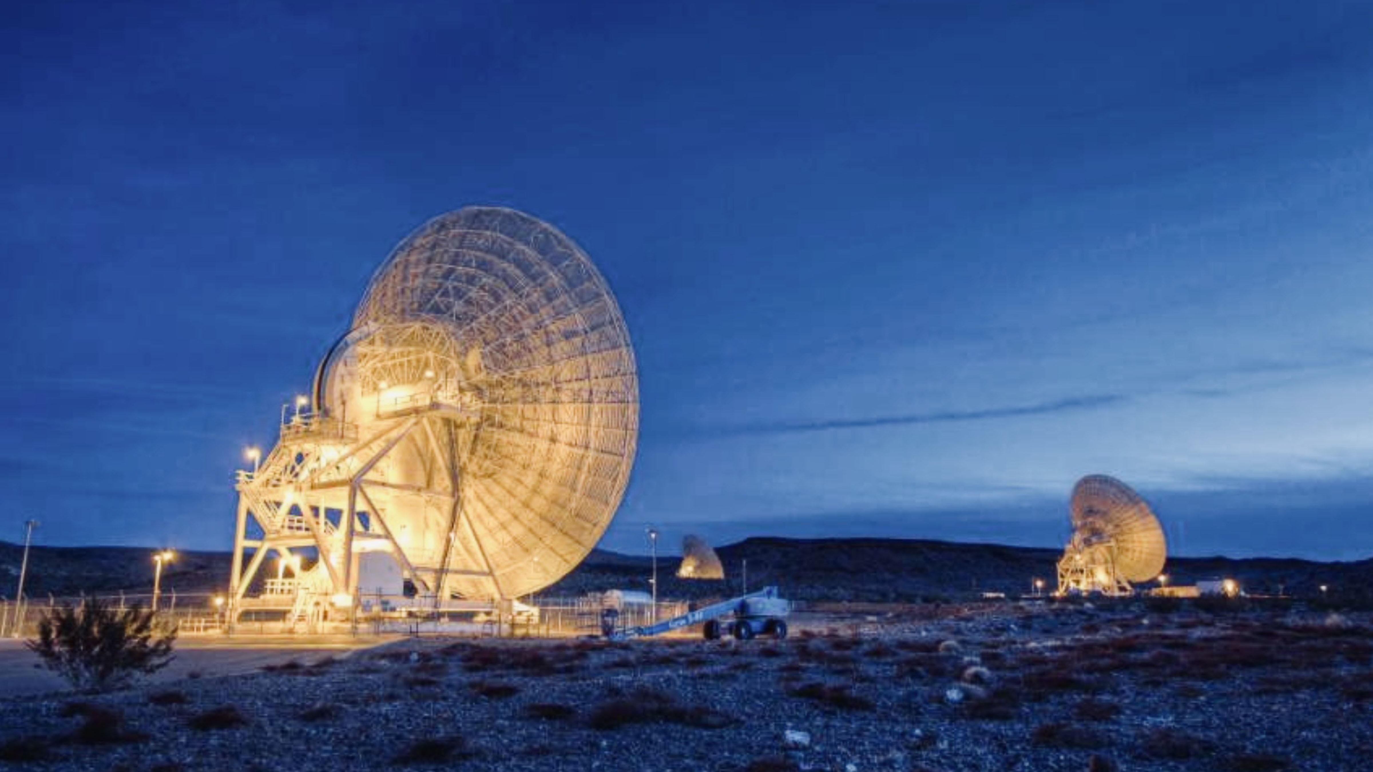 Large radio telescope antennas illuminated at dusk in a remote desert landscape used for deep-space observation and signal detection.