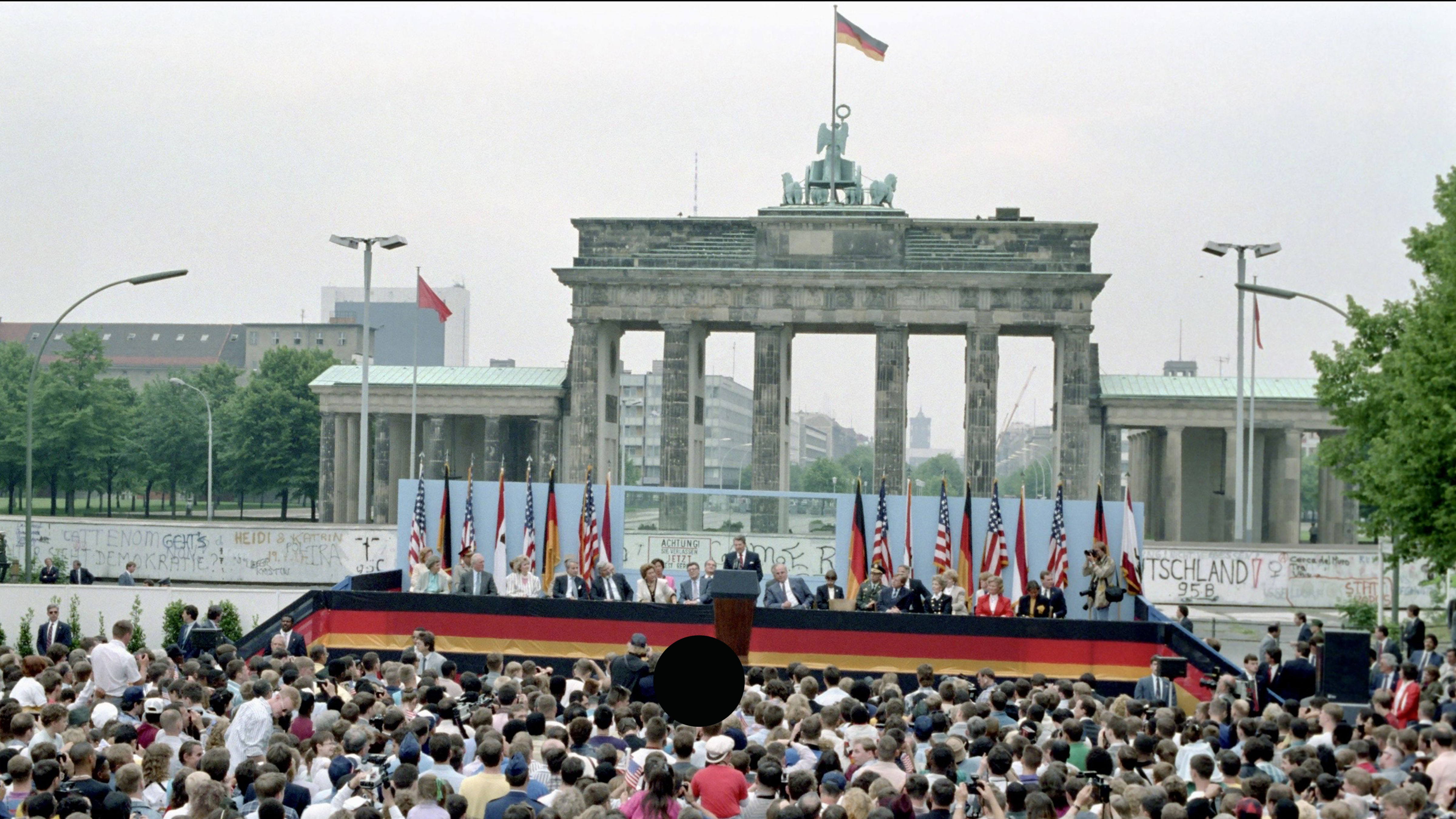 President Ronald Reagan speaks before a large crowd at the Brandenburg Gate in West Berlin on June 12, 1987, with the Berlin Wall visible behind the stage.