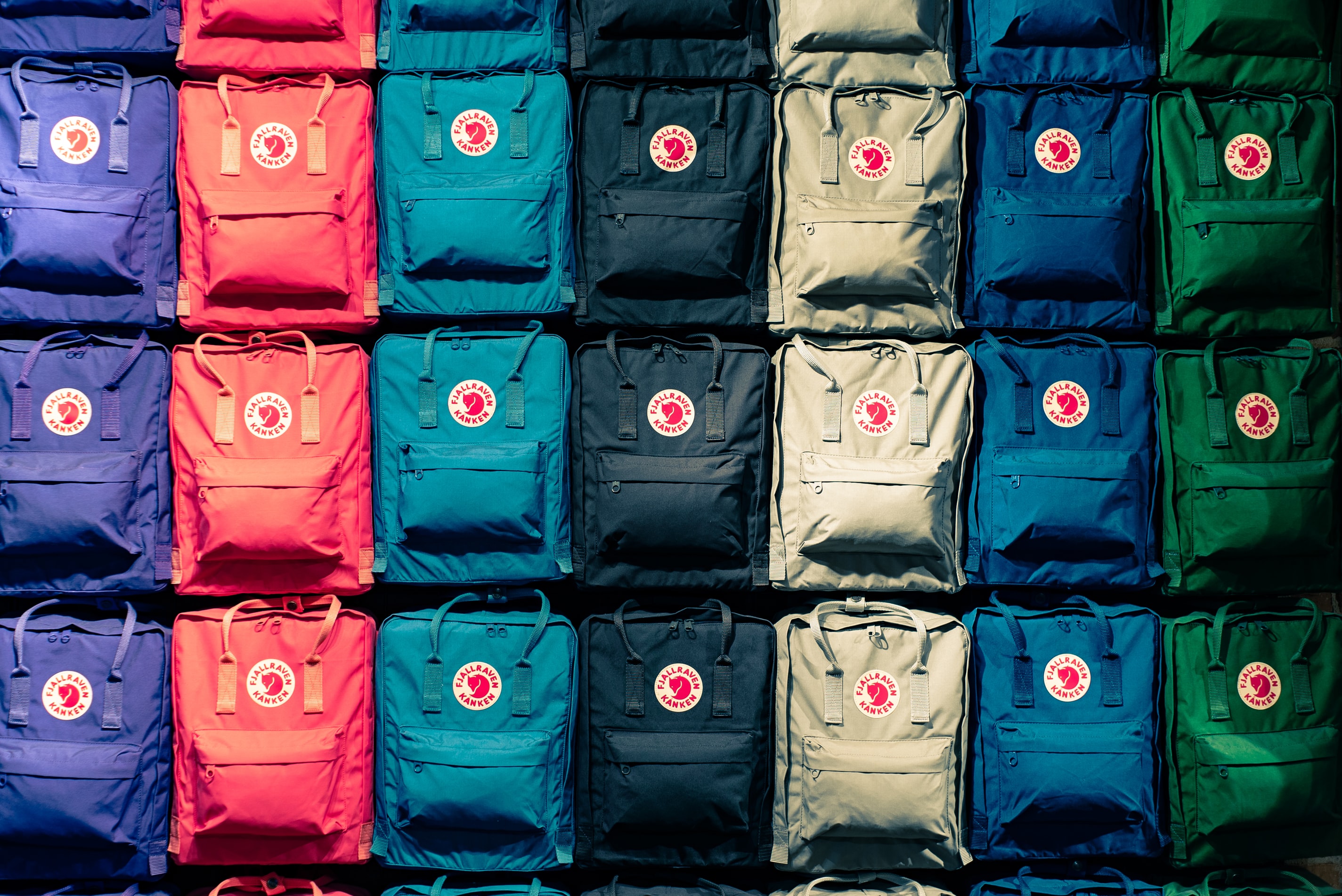 Several backpacks in a range of different colours, placed together to form a cohesive background