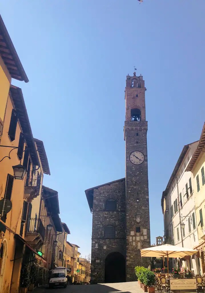 The stone clock tower in Montalcino with a cute street cafe on the right hand side.