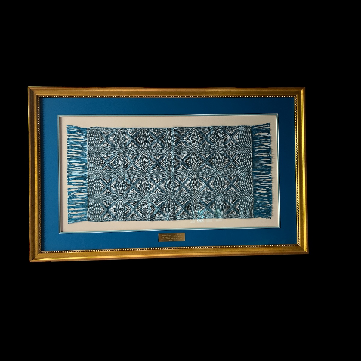 Custom framing of a blue woven tapestry with fringed edges, blue matting, and a gold frame.