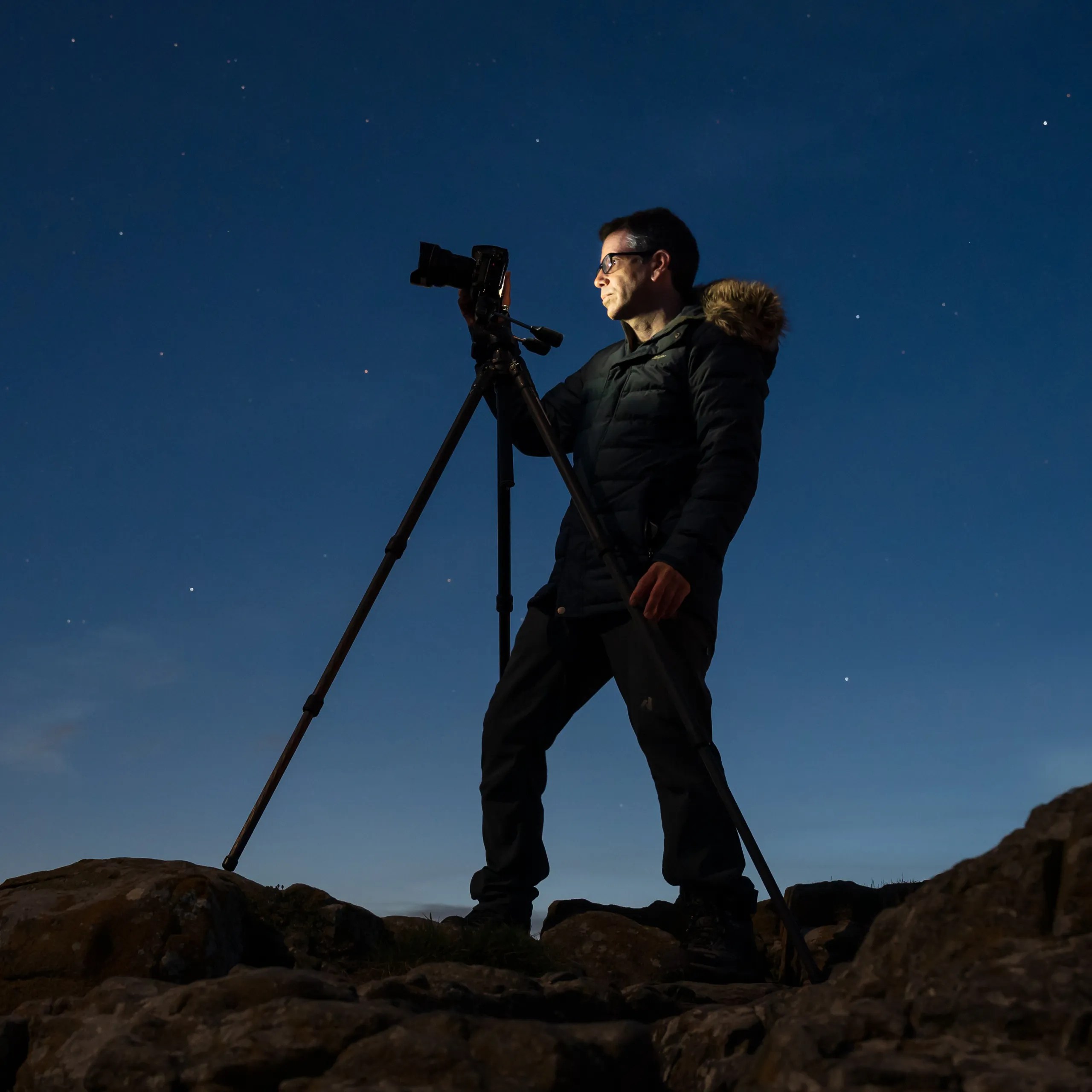 Photographer using a camera and tripod beneath the night sky