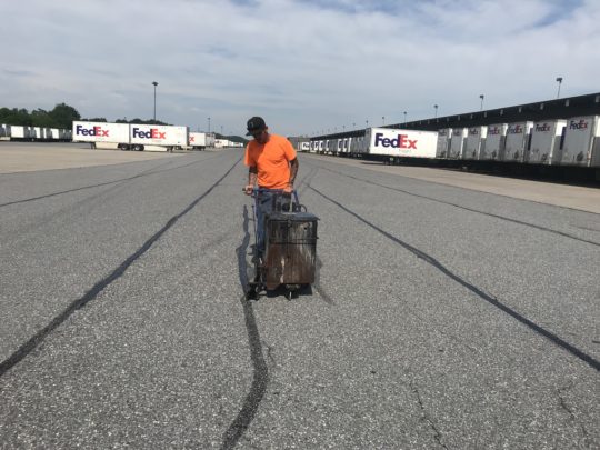 “Applying hot rubberized crack filler to an asphalt road to seal cracks and prevent further deterioration.”