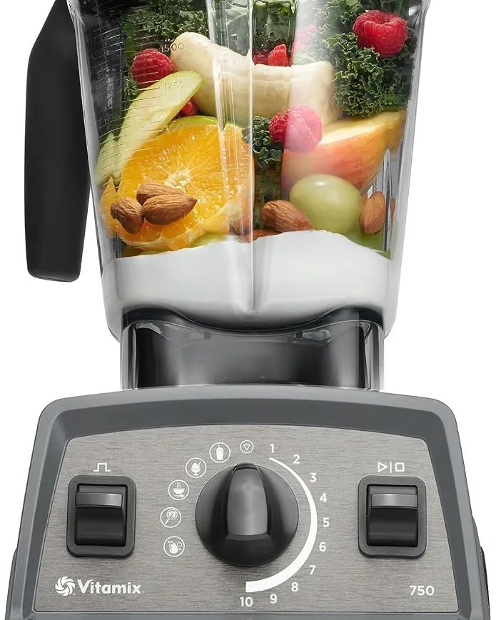 Close-up of a Vitamix blender filled with fresh fruits, vegetables, and nuts, with controls visible on the front.