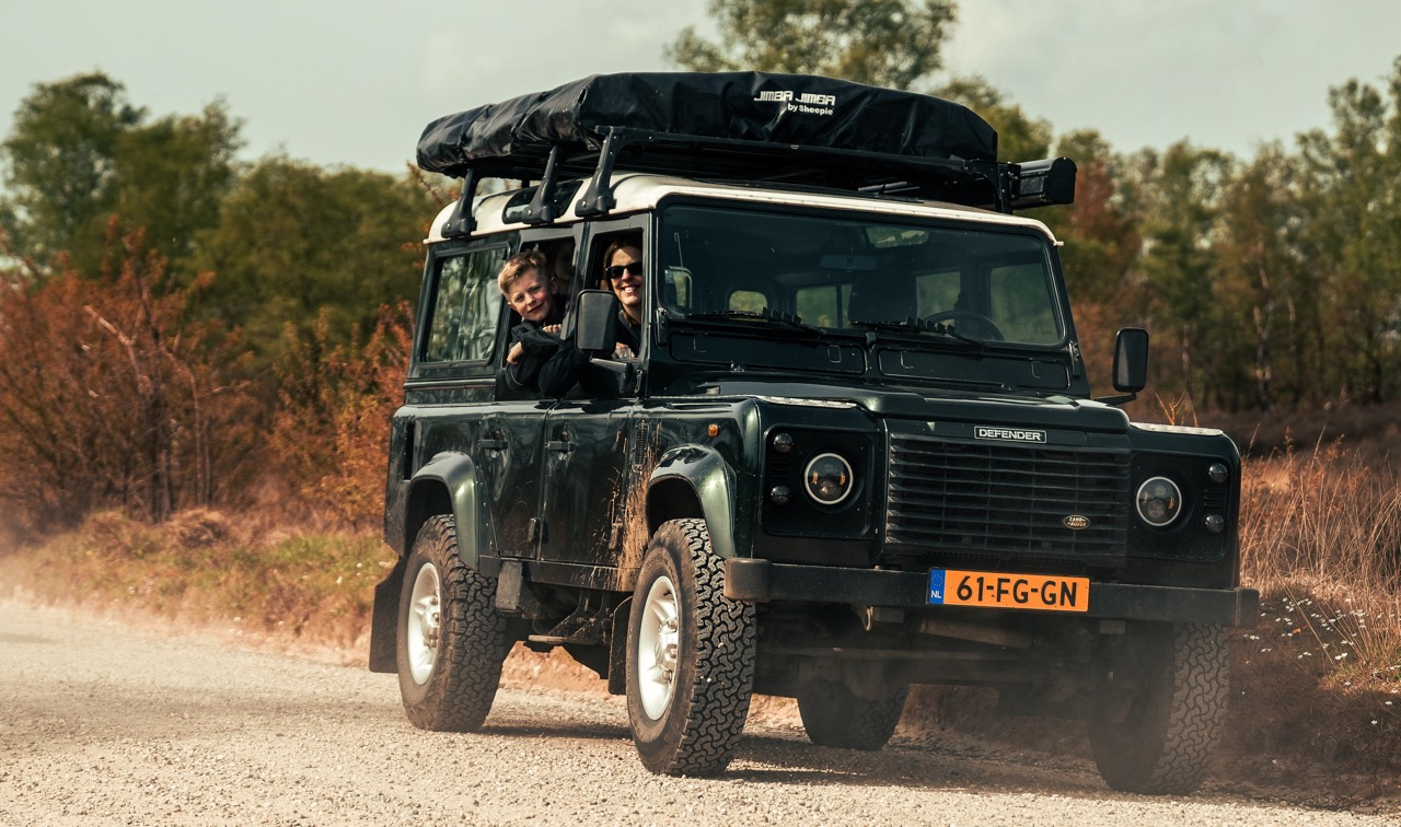 Twee mensen rijden in een Land Rover Defender over een zandweg op de Veluwe, tijdens een offroad tour.