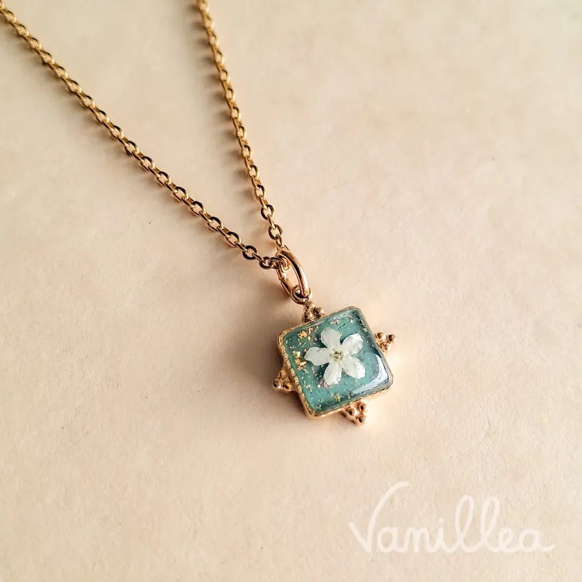 Collier en acier inoxydable doré avec pendentif carré contenant un myosotis blanc naturel.