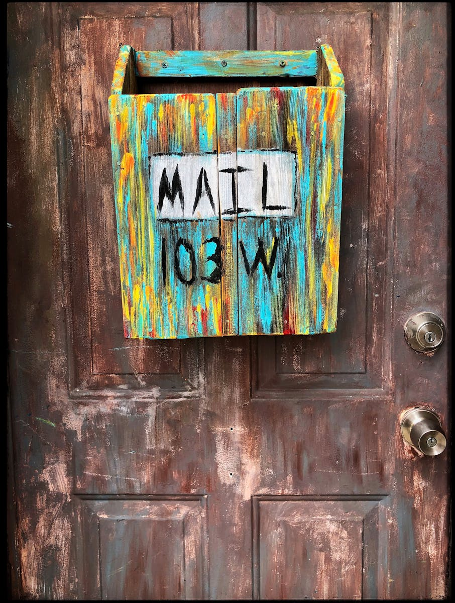 Colorful rustic mailbox labeled 'MAIL 103 W' on a distressed wooden door in Hidalgo, TX.