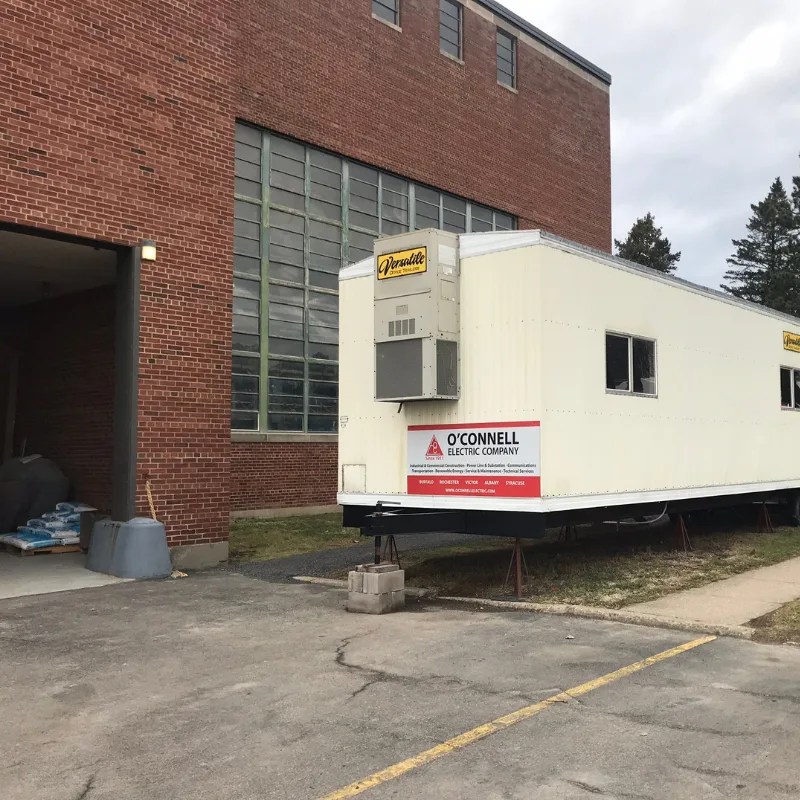 Versatile Office Trailers unit placed beside a brick school or municipal building to provide temporary office space during facility work.