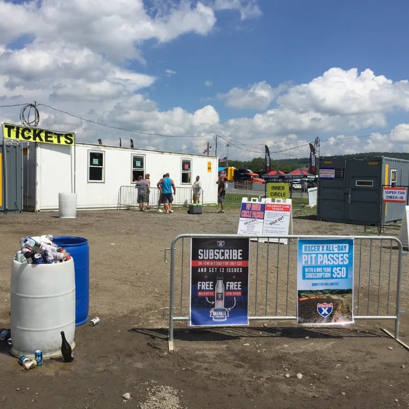 Event-style site entrance with an office trailer labeled “Tickets,” showing organized check-in flow and crowd control barriers.