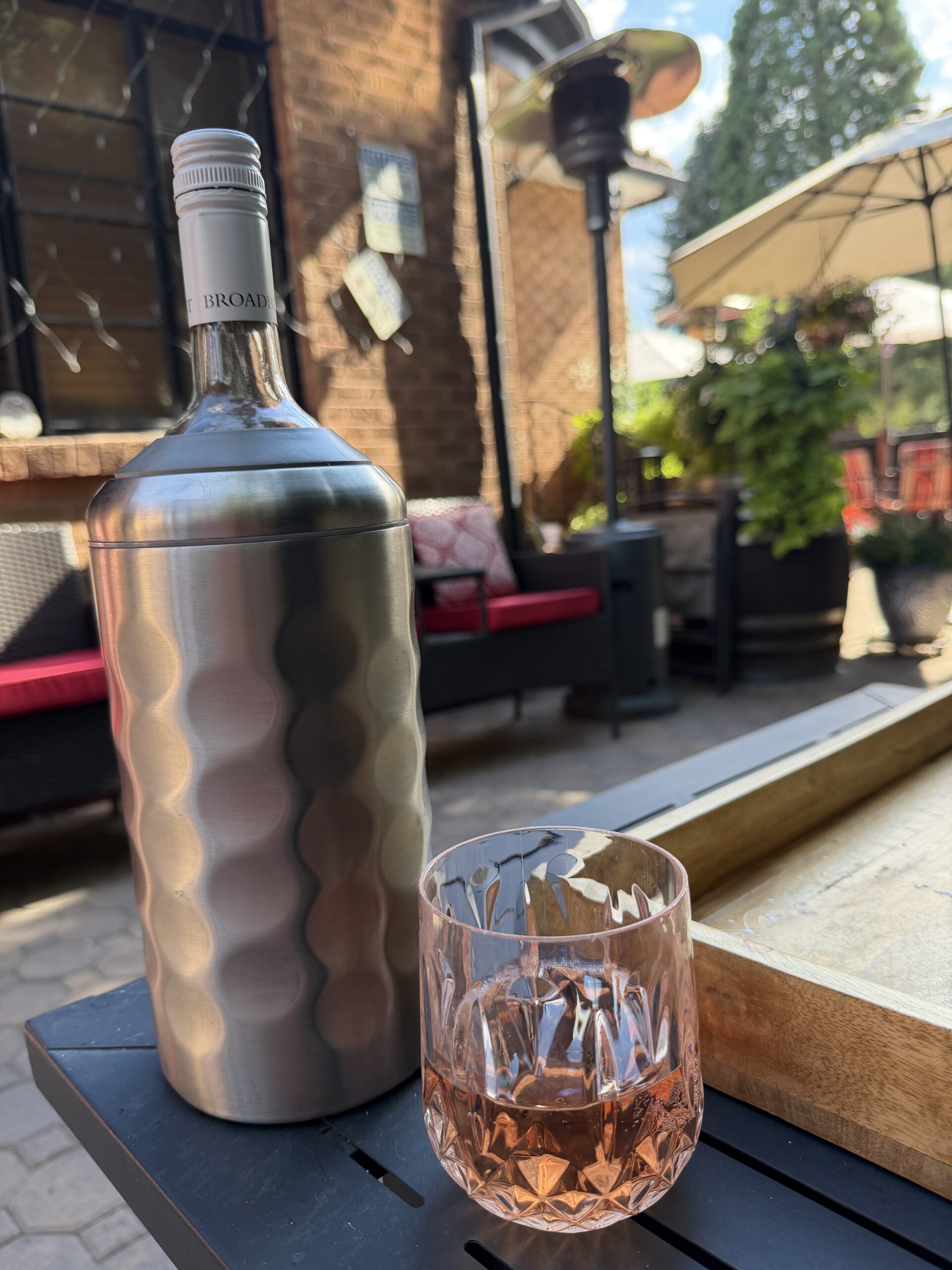 A glass of rosé and a stainless wine chiller on a patio table at Mo's by the River, a wine bar in Reno, Nevada.