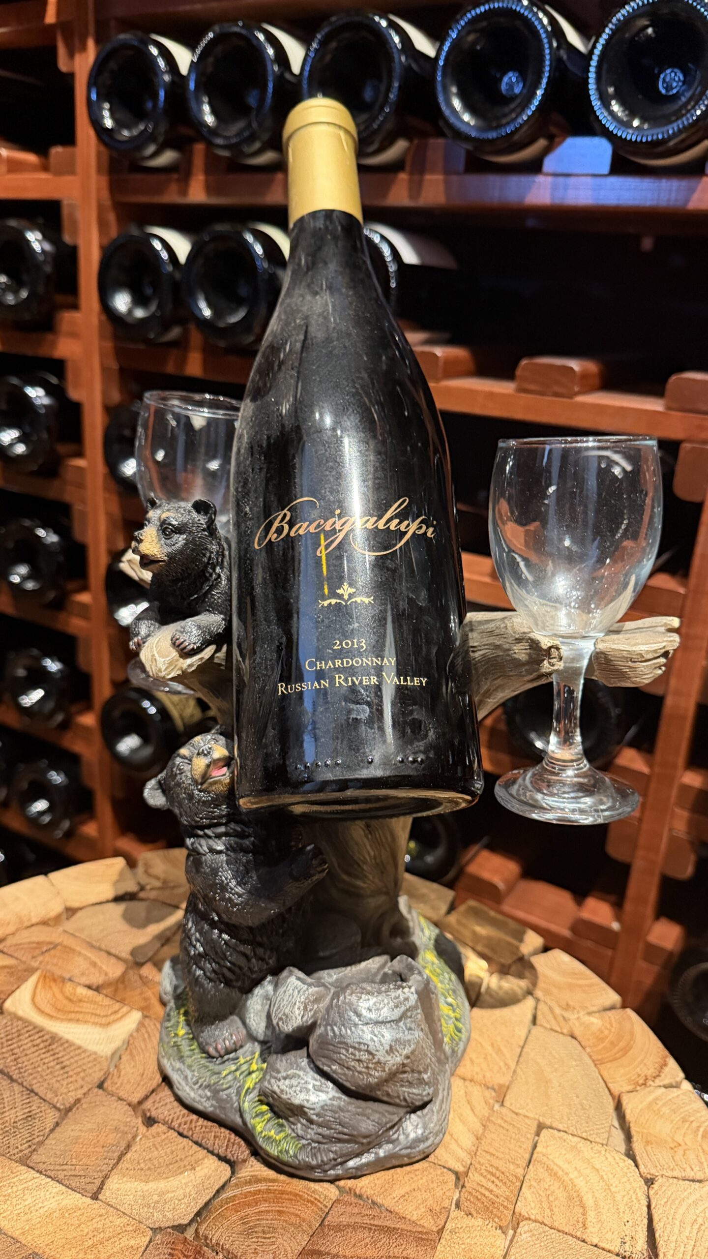 A 2013 Bacigalupi Chardonnay from Russian River Valley on a carved wooden bear holder in a home cellar, kept from a wine club visit worth remembering.