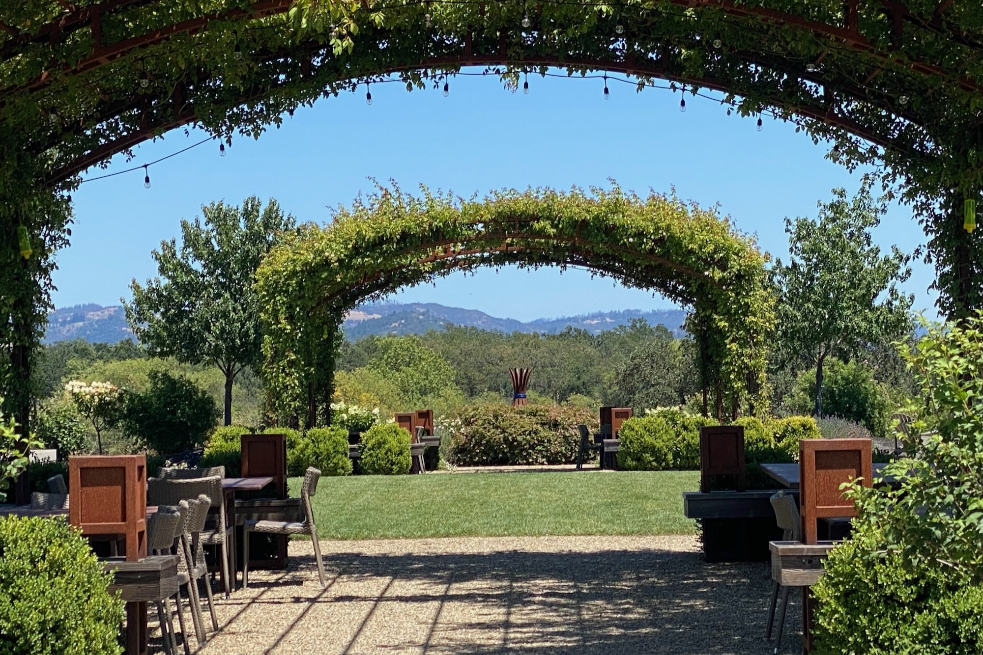 Pergola-covered patio with wooden tables and chairs looking out to vineyard hills