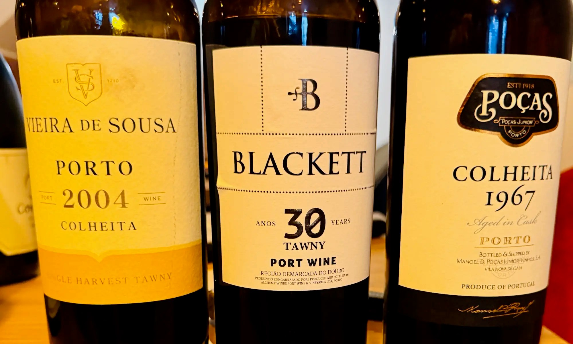 Three bottles of Portuguese port on a wooden ledge in a Porto tasting room, a Vieira de Sousa 2004 colheita, a Blackett 30 Year tawny, and a Poças colheita 1967
