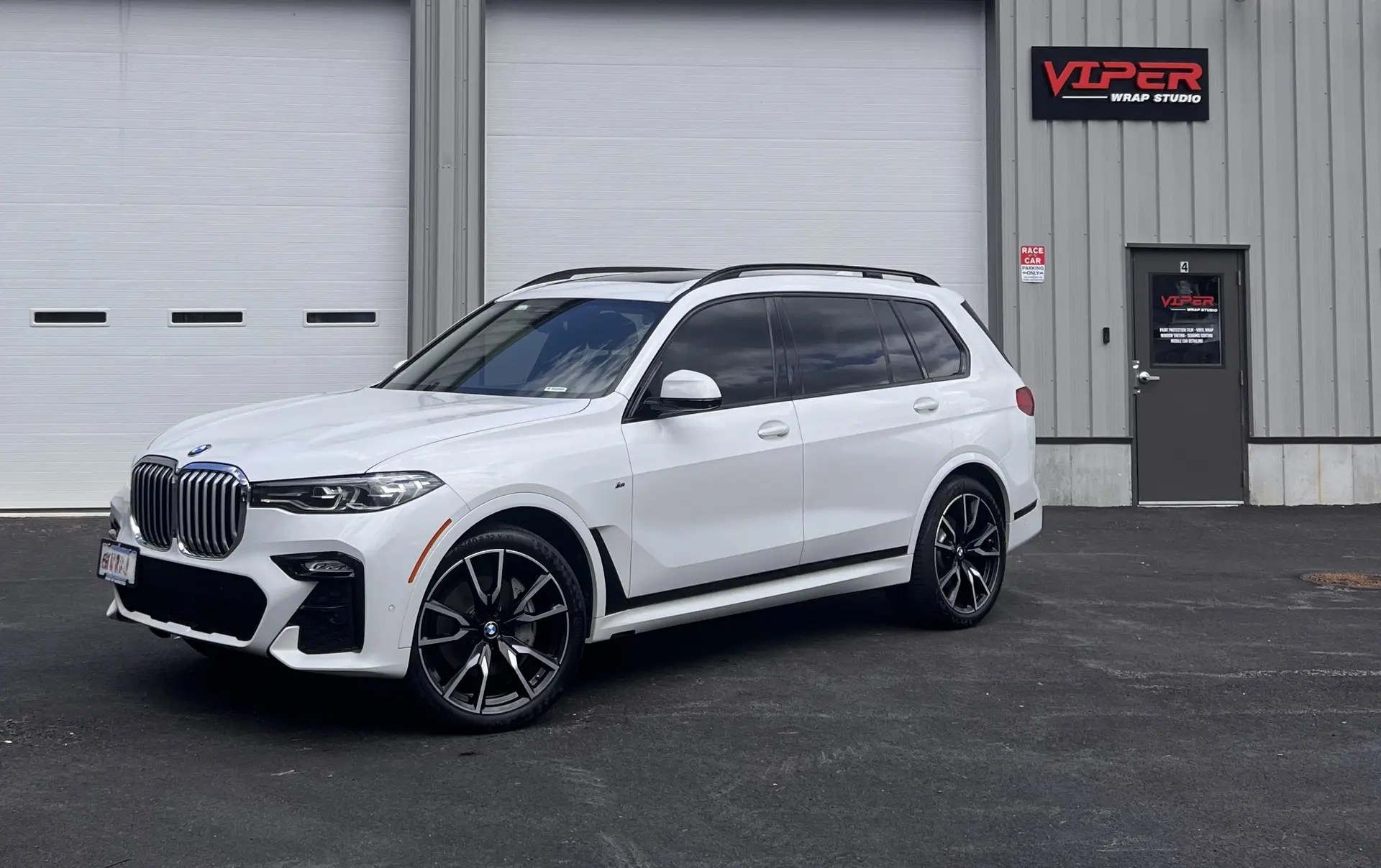 A white 2019 BMW 750i in front of a Auto Shop in Pembroke mass, named "Viper Wrap Studio"