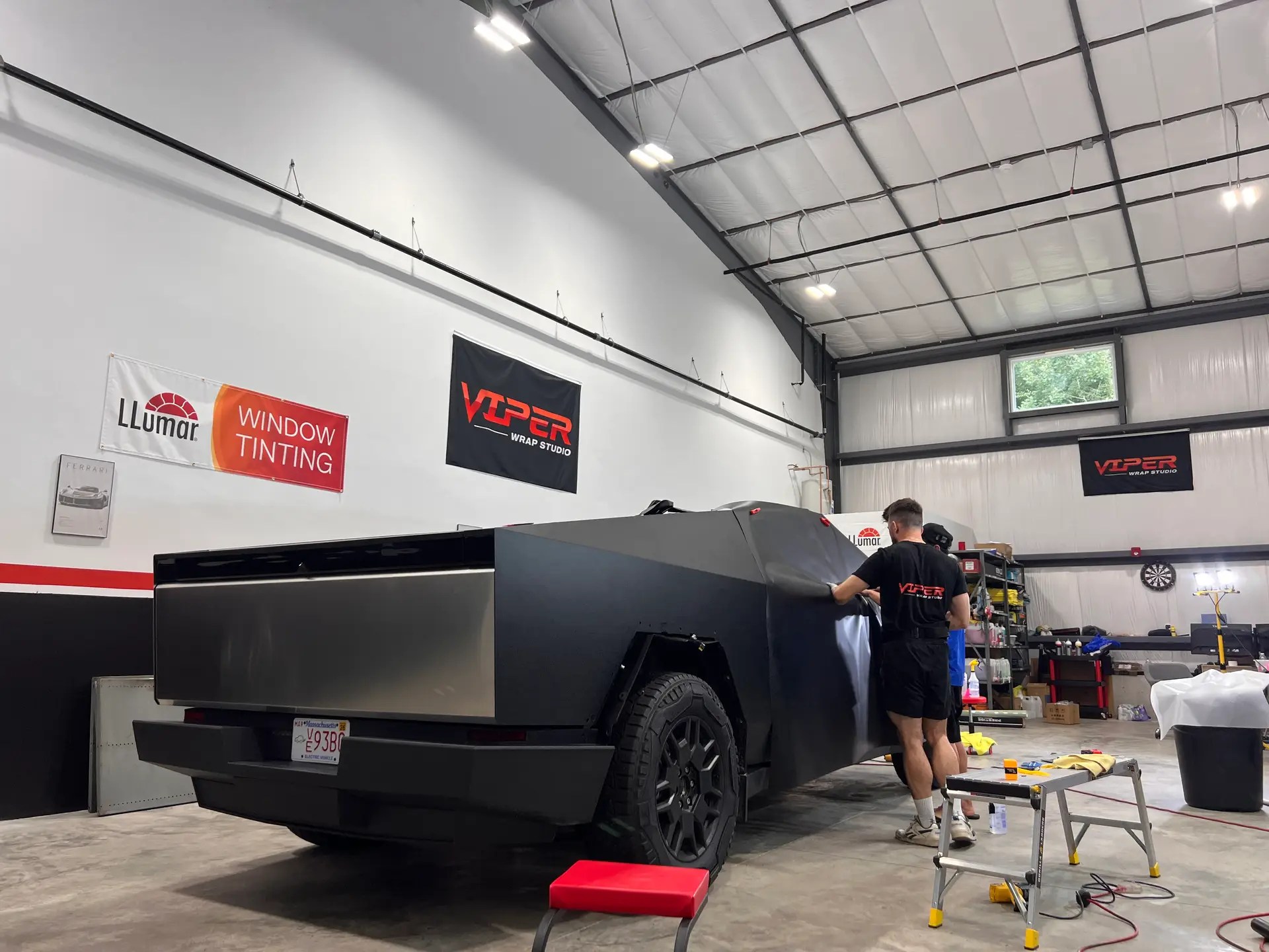 a Cybertruck is being wrap in matte black vinyl inside Viper Wrap Studio, two Viper technicians is working on installing the matte black vinyl wrap