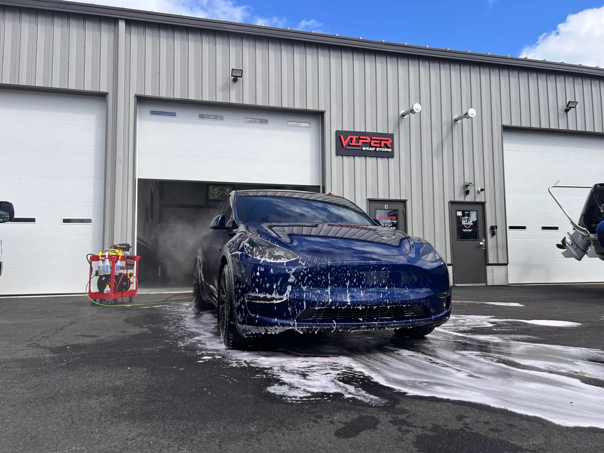 a blue 2024 tesla model y is being detailed by Viper crew in front of Viper wrap studio & car detailing, services include: Auto detailing, window Tint, ppf, and vinyl wrap.