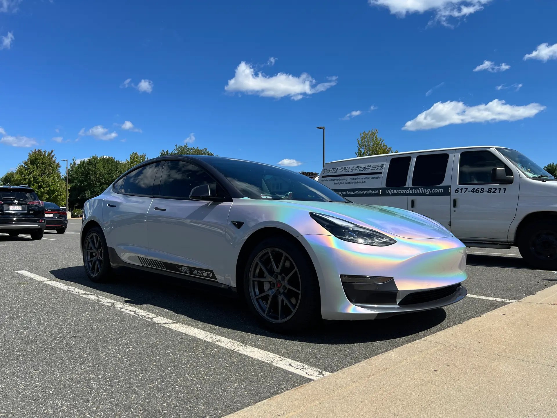 a fully wrapped tesla model 3 parked next to viper car detailing mobile van in a parking lot