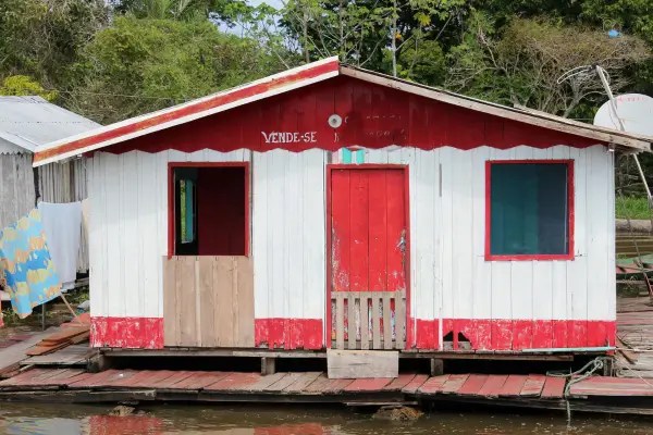 Casa ribeirinha sobre estrutura de madeira às margens de um rio na Amazônia.