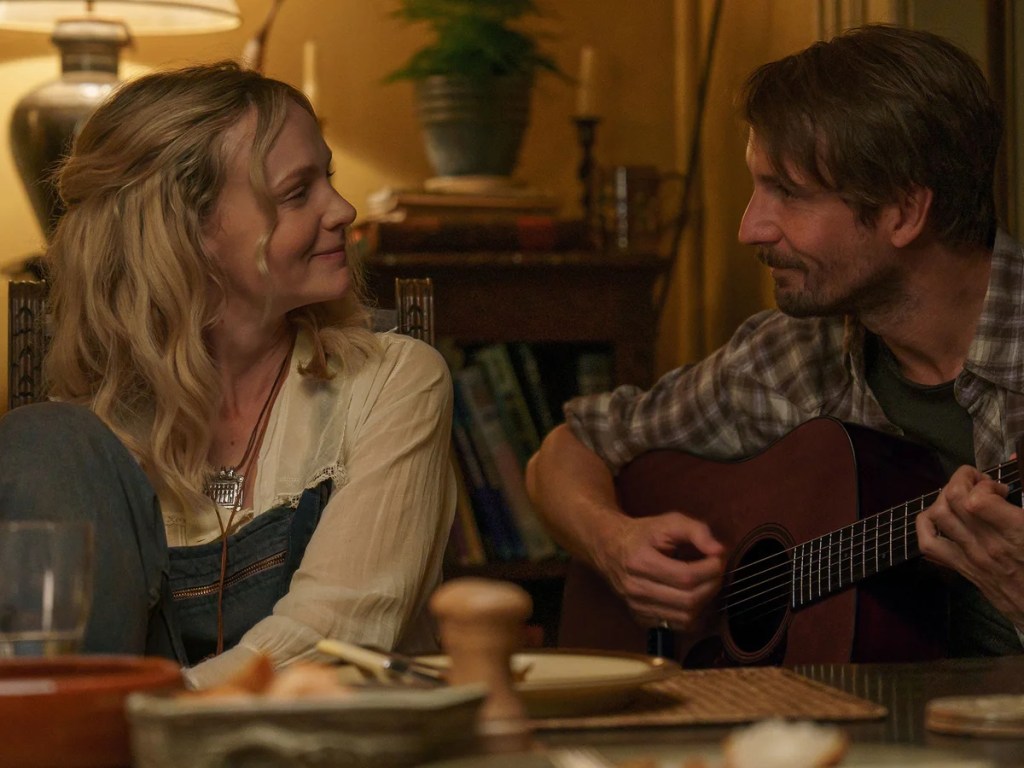 Events in Hexham. Promotional image for The Ballad of Wallis Island. Blonde woman smiling at a dark-haired, bearded man who is playing the guitar.
