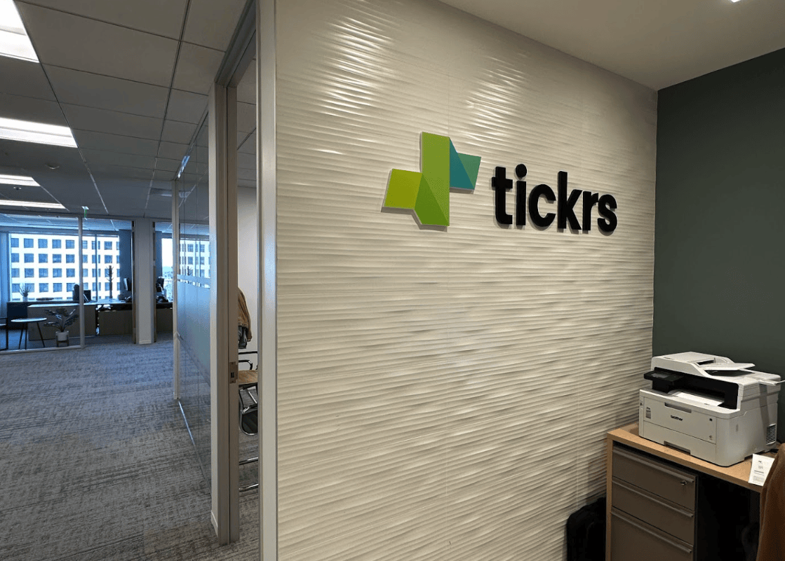 Tickrs custom dimensional logo wall sign installed on textured office wall