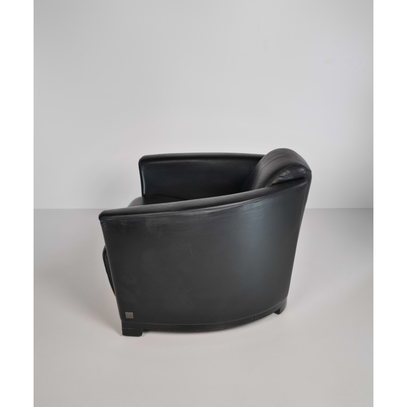 Black leather lounge chair with a rounded back in a minimalist white studio.