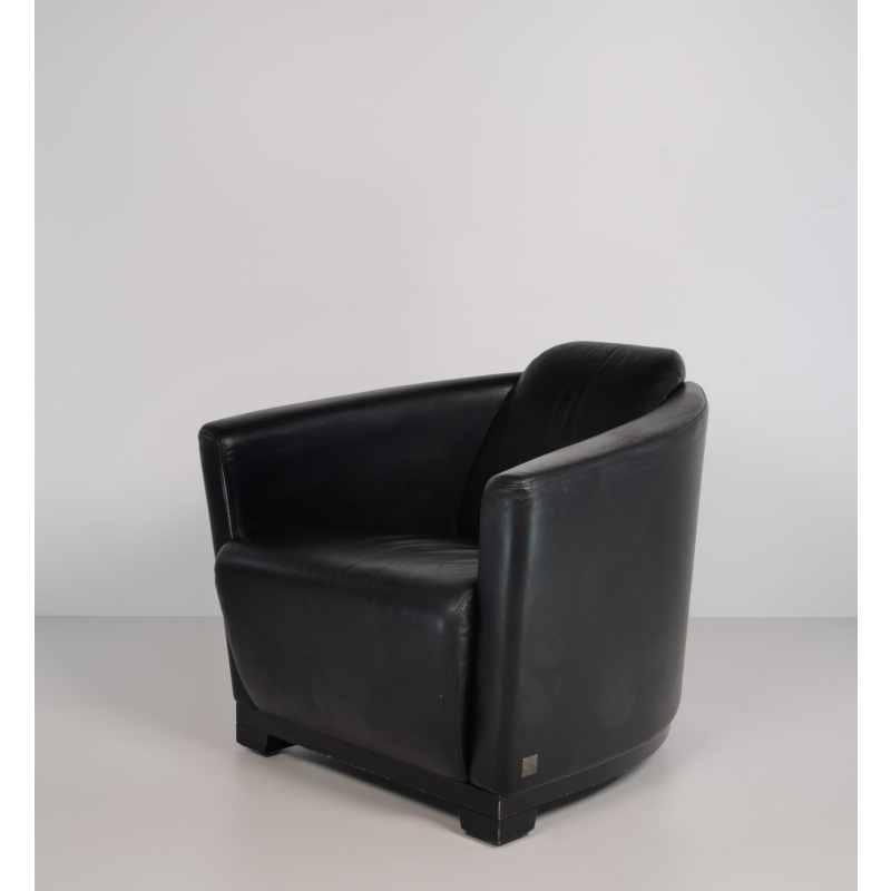 Black leather armchair in a minimalist studio setting with a light gray wall and floor behind it.