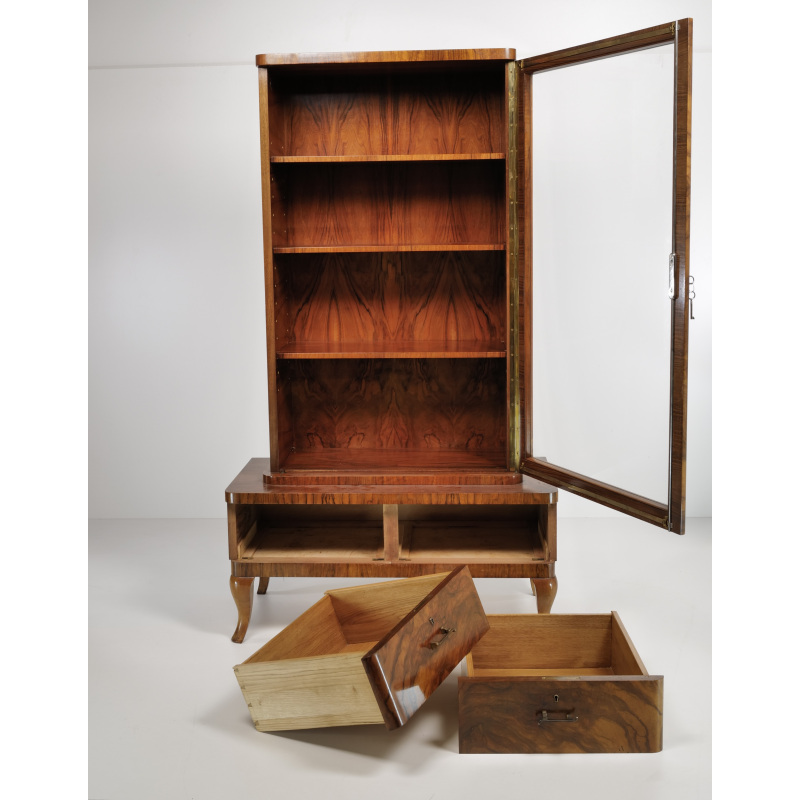Wooden display cabinet with glass door open, showing five shelves and a lower storage area with two drawers; several drawers pulled out in front.