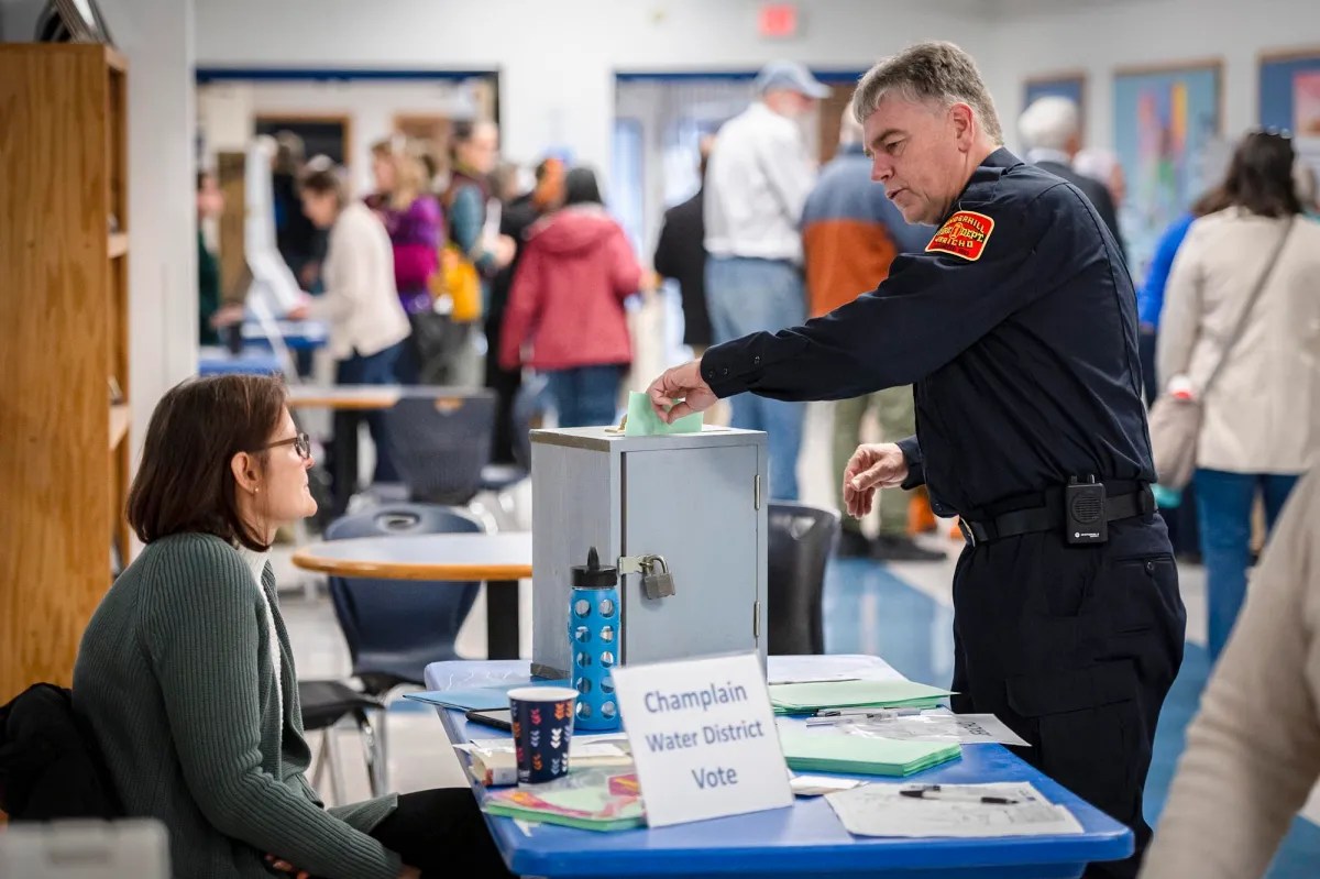 A police officer handing out a ballot to a woman in a classroom.