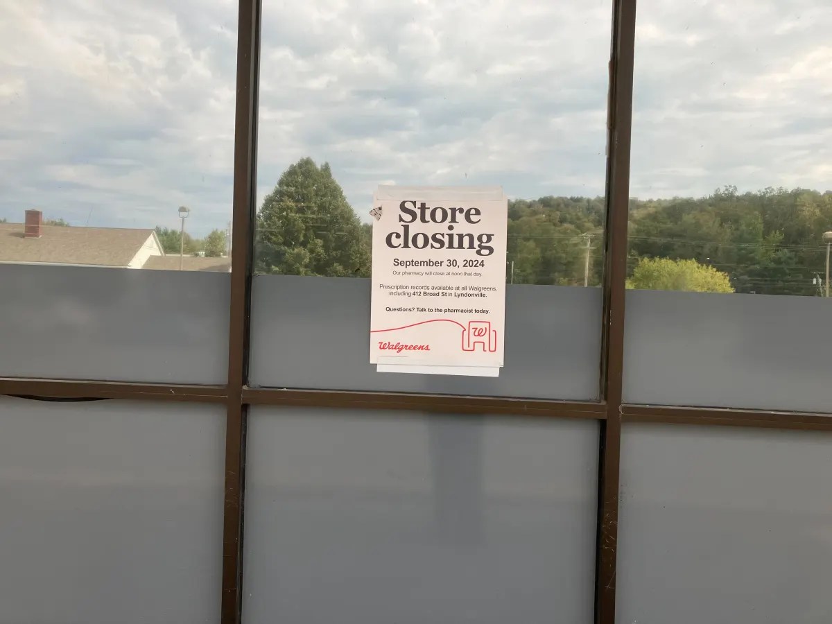 Sign on window announces a store closing on September 30, 2024, with transfer details to a nearby store. Trees and a cloudy sky are visible outside.