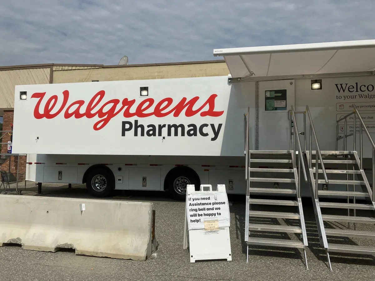 Mobile Walgreens pharmacy unit with stairs and a sign offering assistance, parked in an open area.