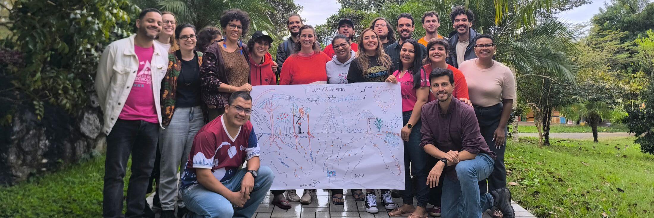 A group of men and women in a loose huddle outside display a colorful drawing with enthusiasm