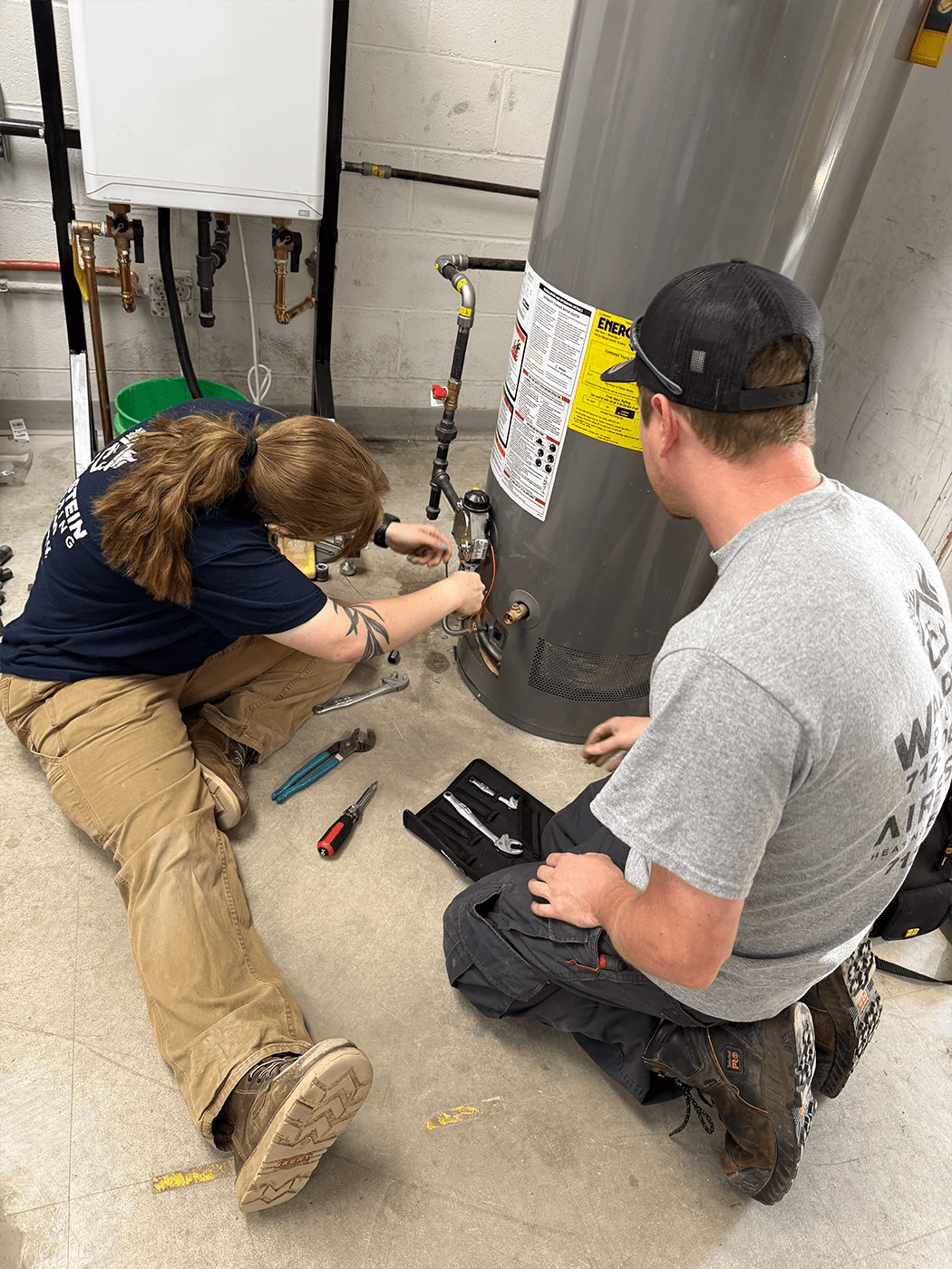 Two people on the ground working on a water heater