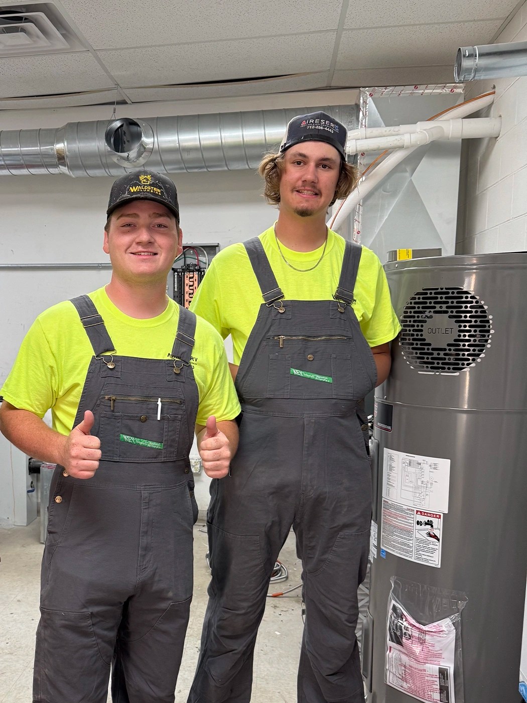 Two men in overalls next to a water heater